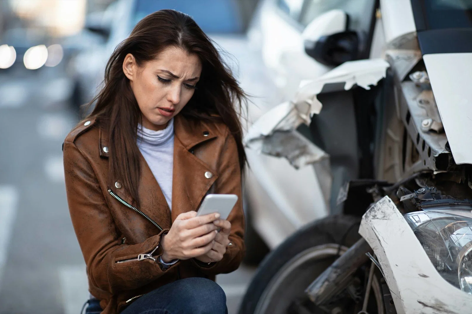 Woman checking her phone beside a crashed car on a New York street