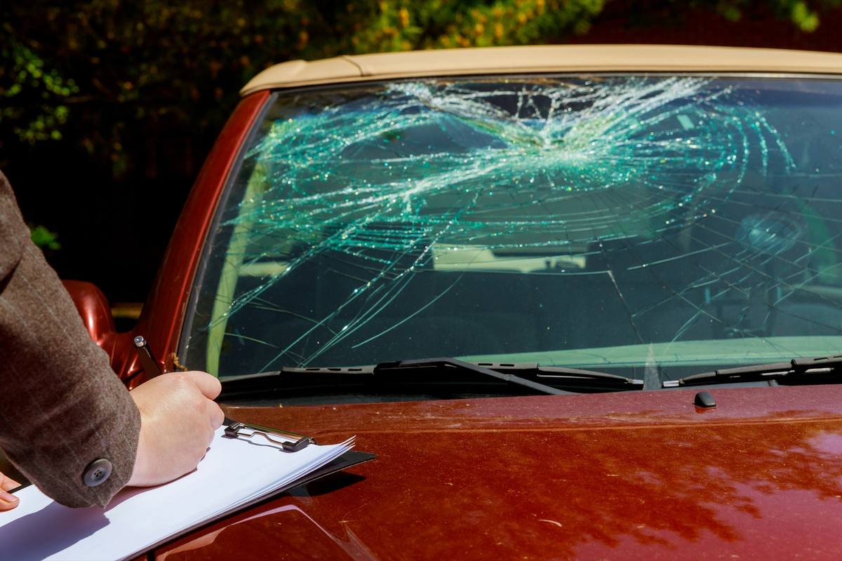 Insurance paperwork on a clipboard resting against a shattered windshield