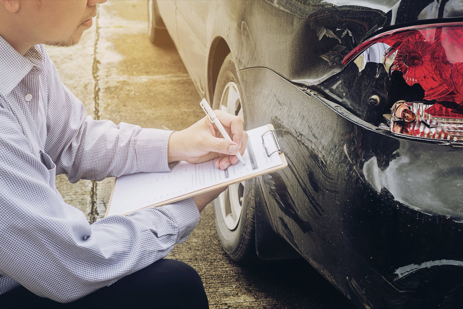 Insurance agent writing on a clipboard beside a shattered taillight