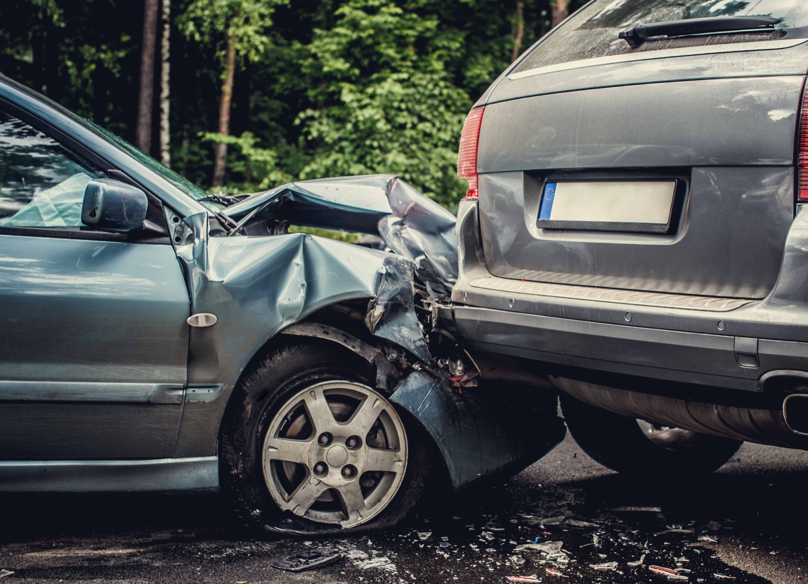 Two cars locked together after a head-on collision on a wooded road