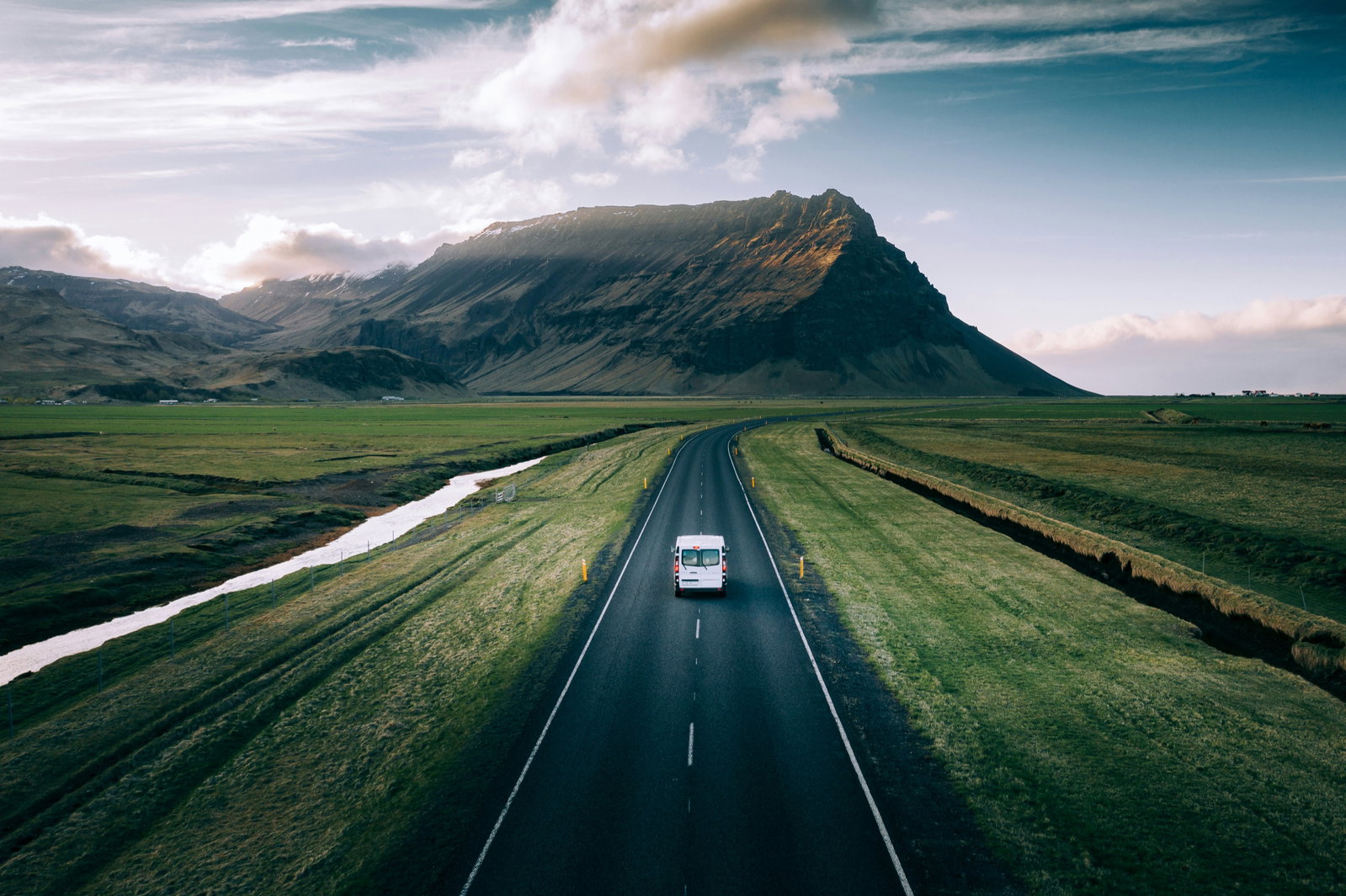 Van driving an open road toward a mountain under a bright sky