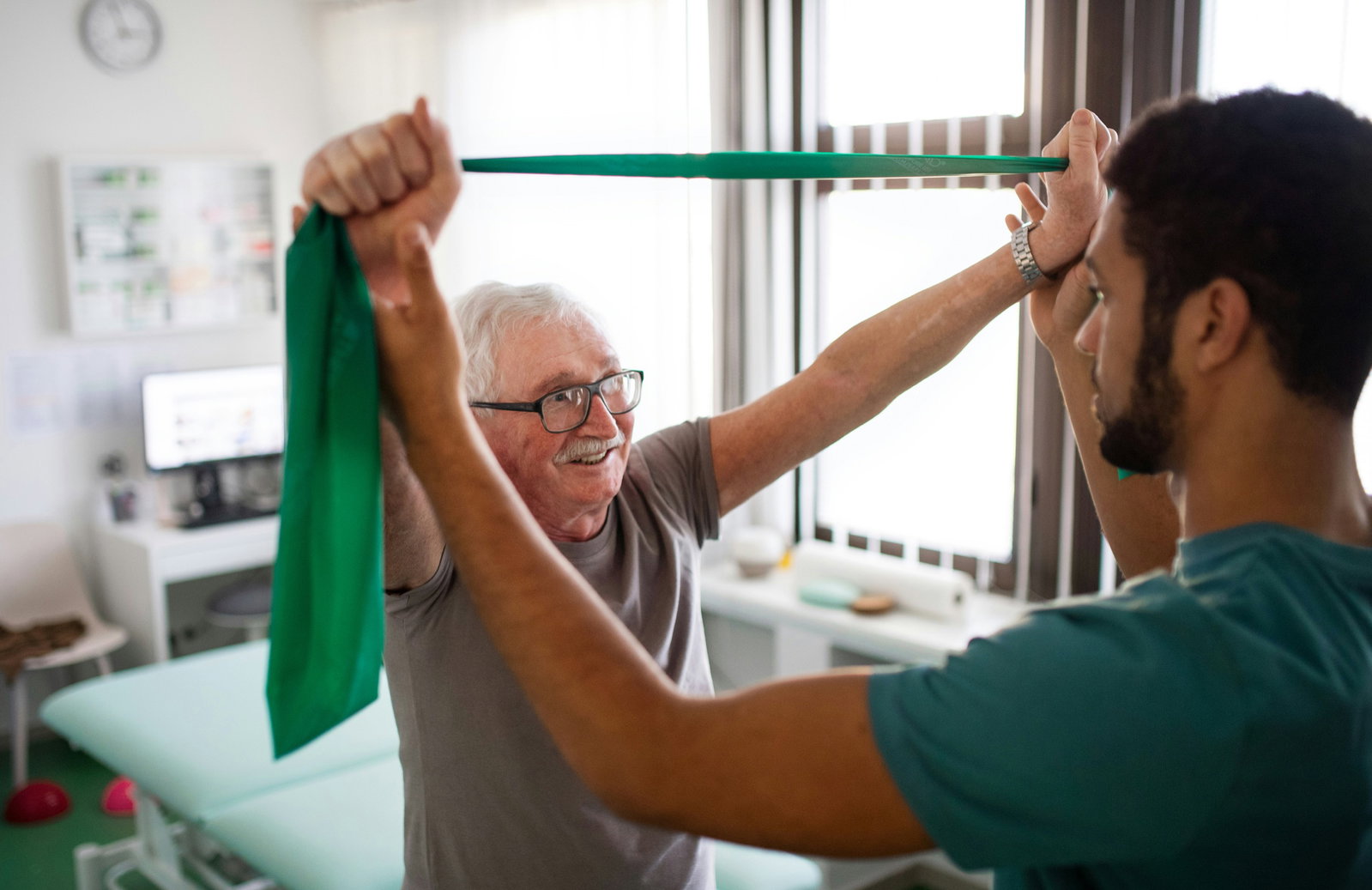 Smiling older man doing overhead resistance-band exercises with his therapist