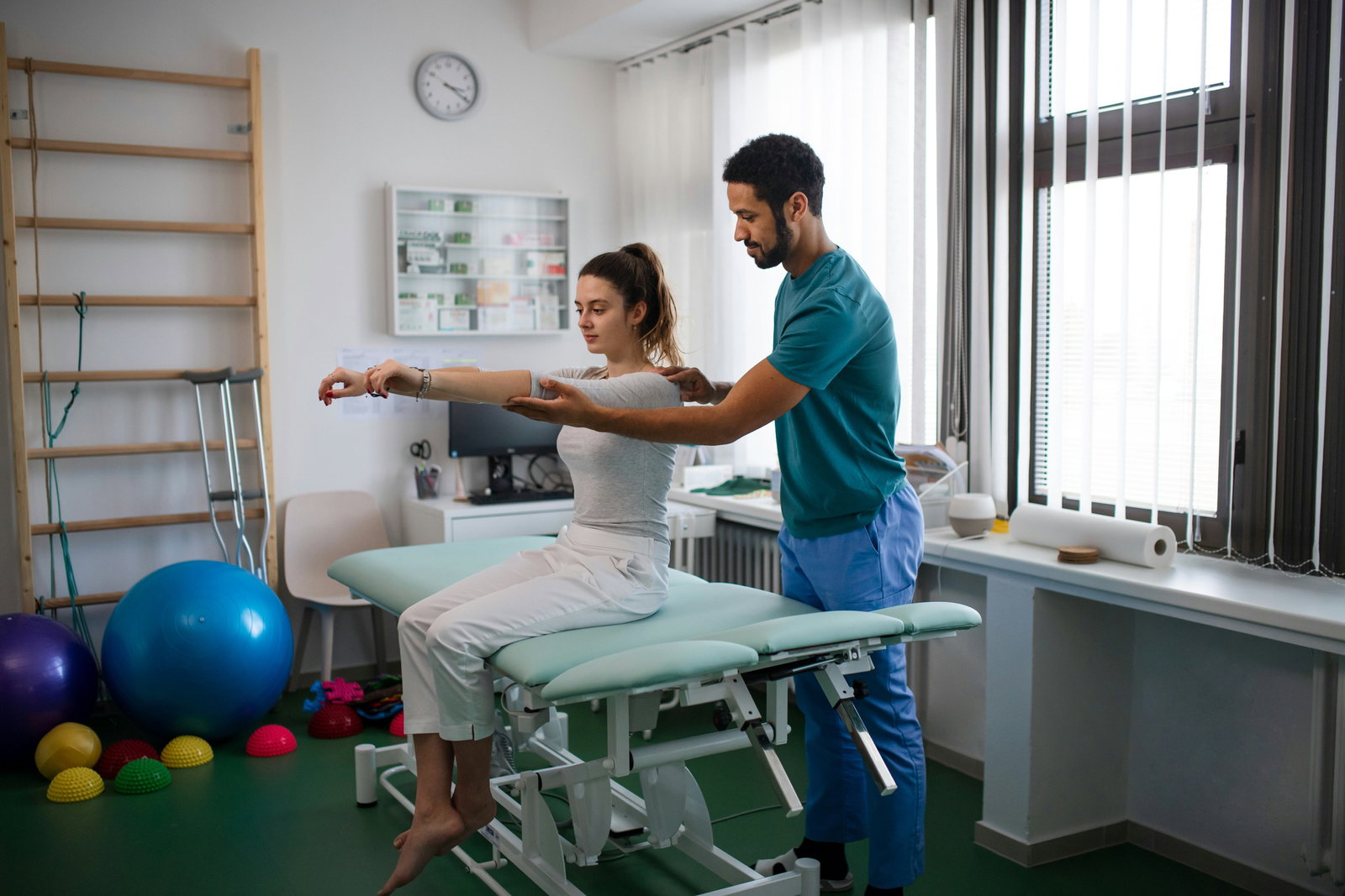 Physical therapist guiding a young woman's arm raises in a bright clinic