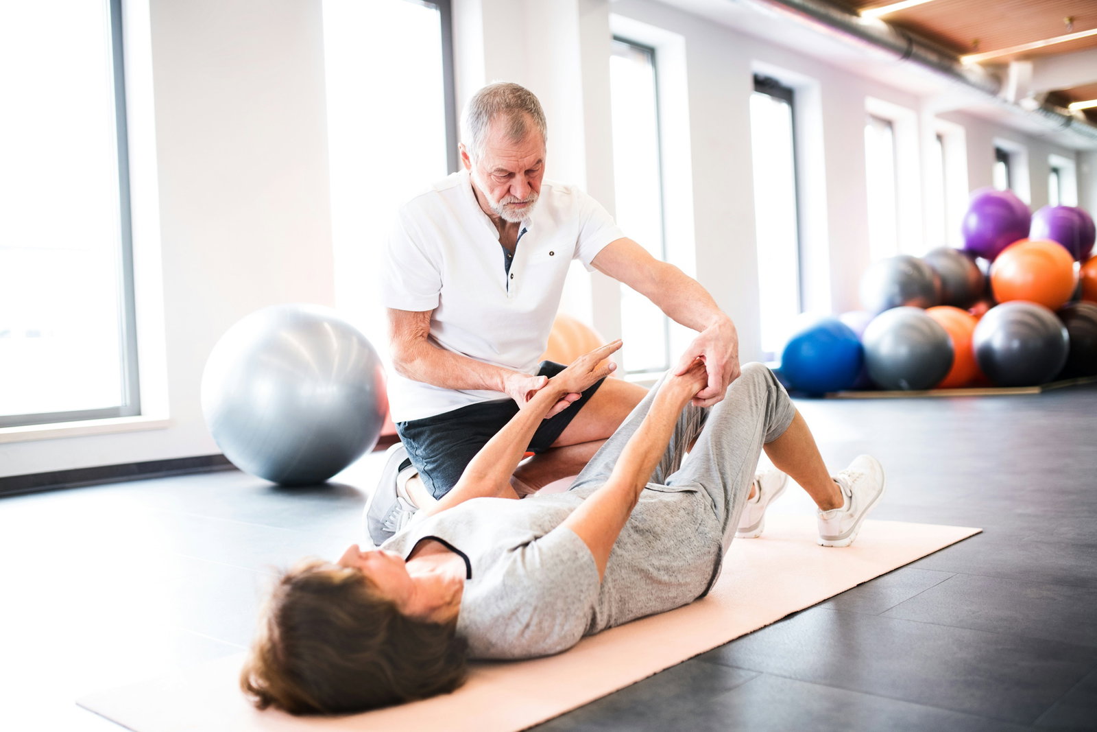 Physical therapist guiding a patient through a floor exercise in a bright rehab gym